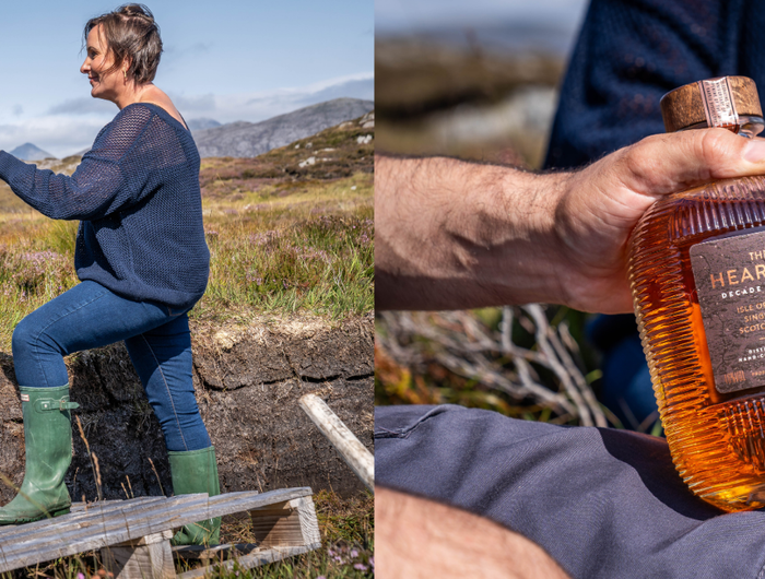 Two people sitting outdoors with a scenic background, one holding a bottle of Hearach Decades edition whisky.